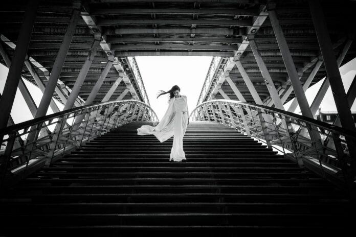 Stylish woman in white posing dramatically on a French bridge.